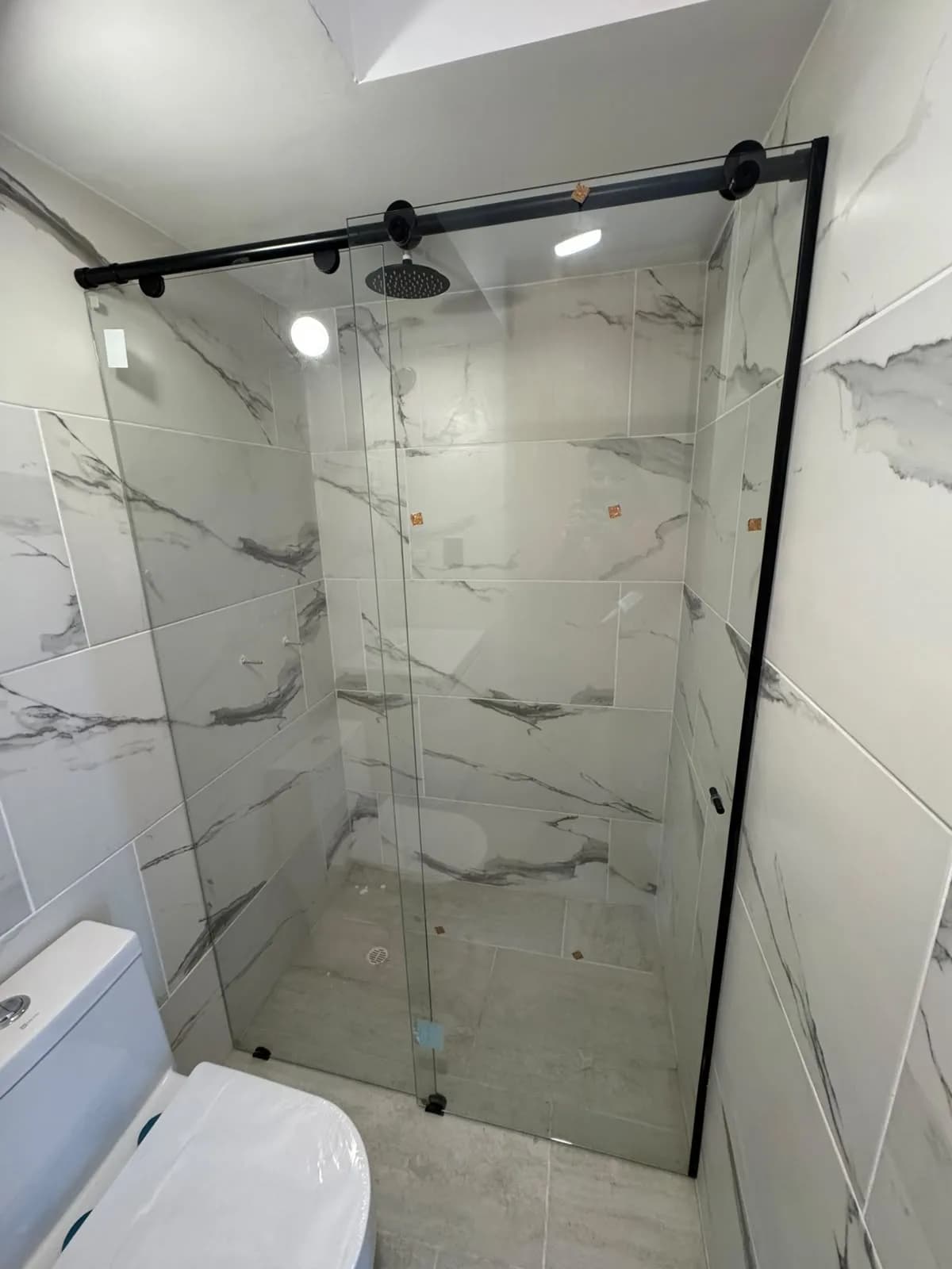 Baño terminado con ducha enchapada en mármol y mampara corrediza de perfil negro