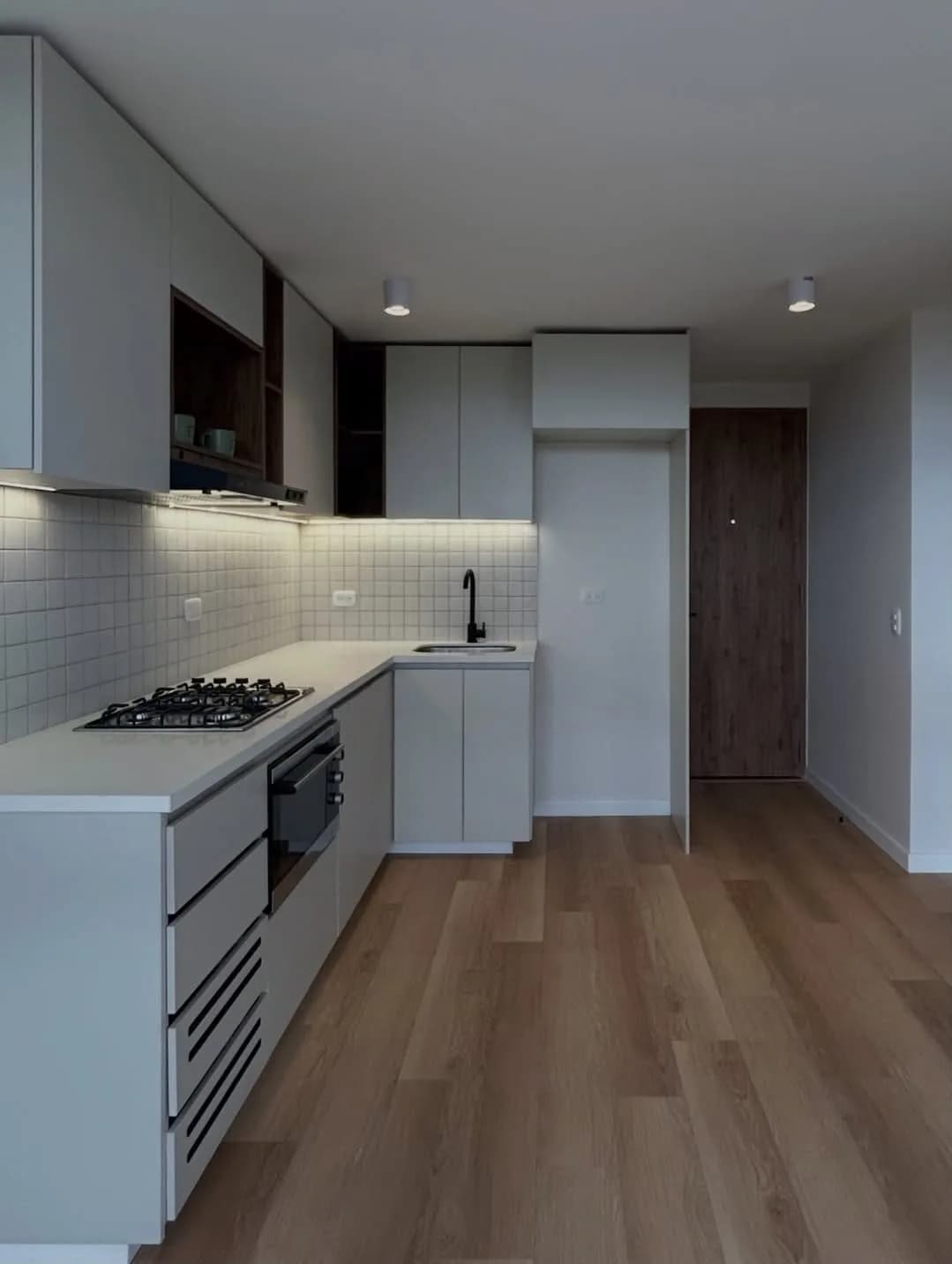 Cocina terminada en blanco, en escuadra, con enchape metro y luz bajo la alacena