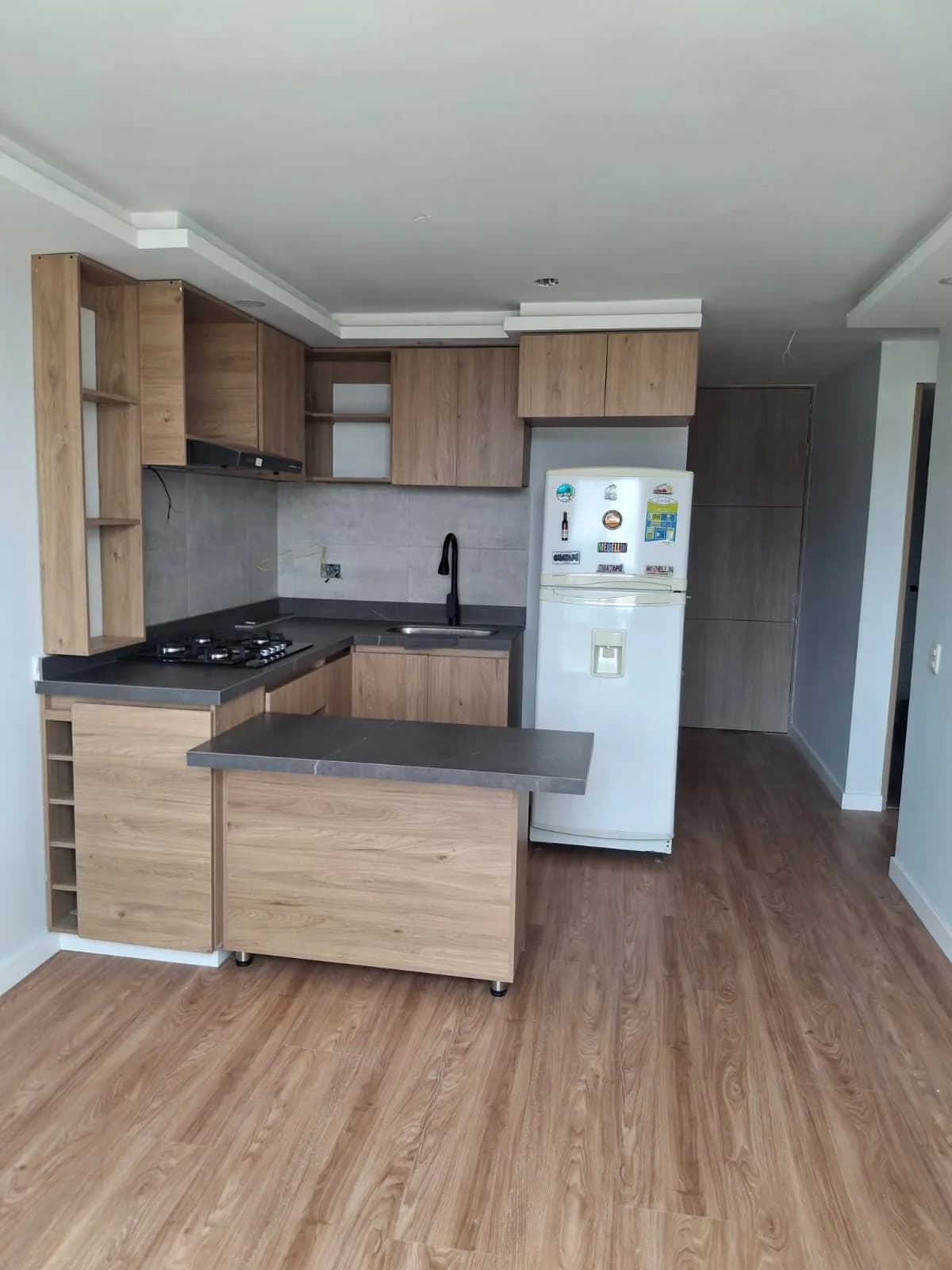 Cocina terminada en madera, con península y mesón oscuro, en un apartamento vacío